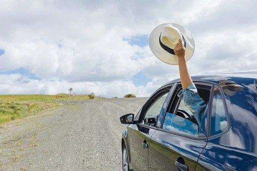 Personne au volant d'une voiture agitant un chapeau